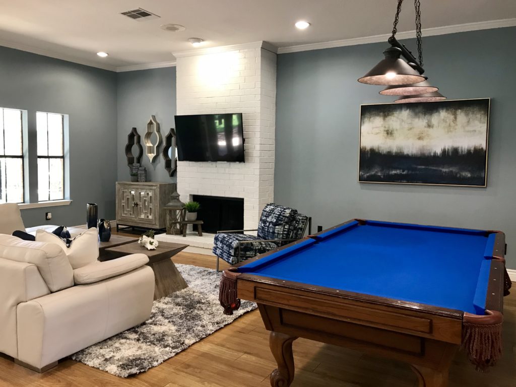 Living room in neutral tones with a fireplace and pool table on the side 