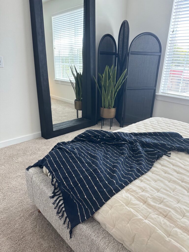 Bedroom staged with finishing touches including a standing mirror, plant and blanket