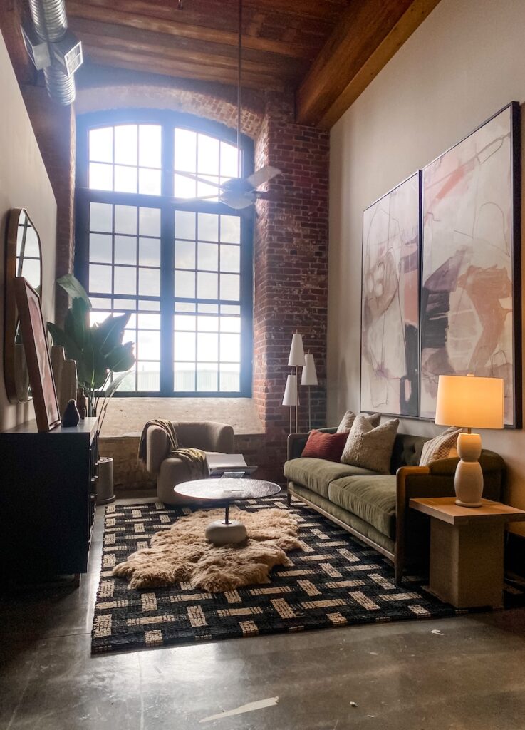 Living room with exposed brick, wooden ceiling and large artwork above sofa in this furnished model apartment