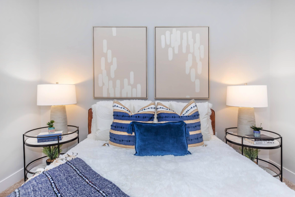 Close up of bed with blue pillows and light abstract artwork hanging above the bed