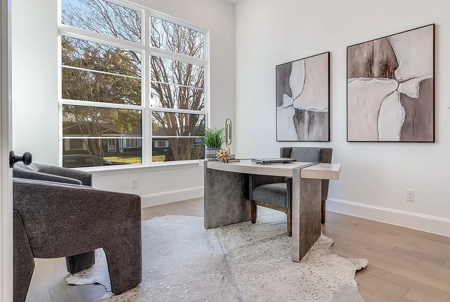 A study in a a Dallas home staged with a modern sleek desk, grey high back desk chair, two dark grey guest chairs and abstract art