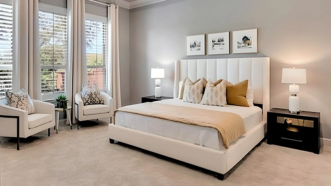 Bedroom with large white upholstered bed, white bedding, two black nightstands with white lamps and two white boucle chairs next to windows