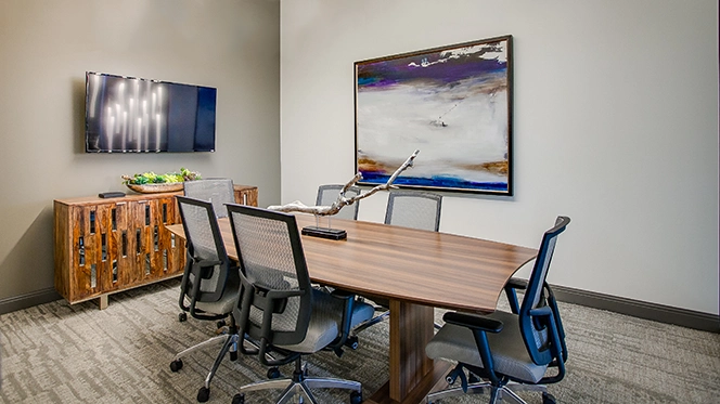 Conference room with rectangular wooden table, six mesh high back chairs, wooden console with tv