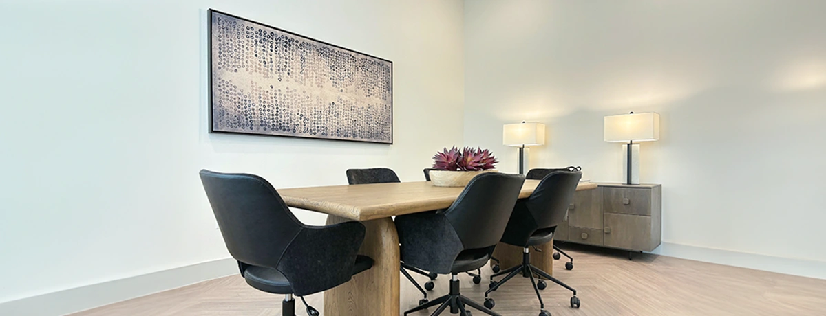 Conference table with light wood and six black leather low back chairs