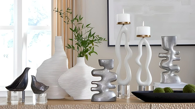 A mix of modern home decor elements with white vases, white wavy candle holders, silver wavy accents and greenery