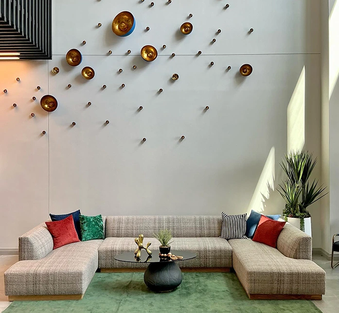Large leasing area with a U-shaped sectional sofa, red, blue and green pillows and circular metal art pieces above sofa