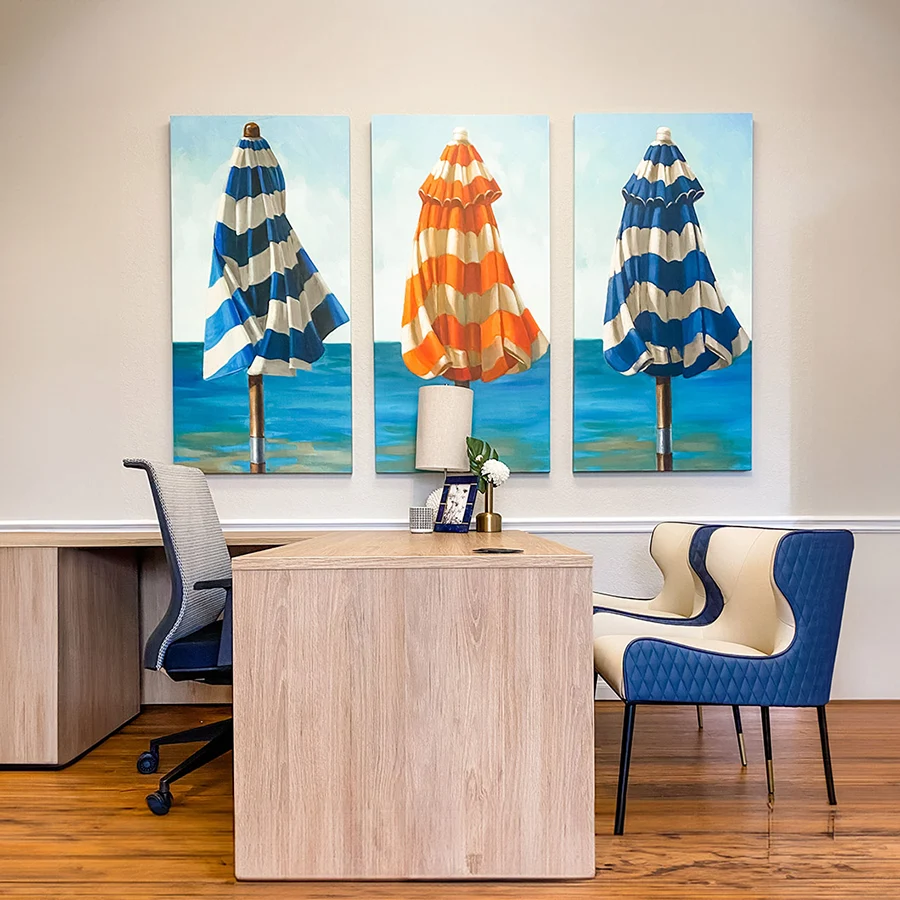 Leasing office with light wooden l-shaped desk, blue and white guest chairs and three umbrella artwork pieces in blue and orange