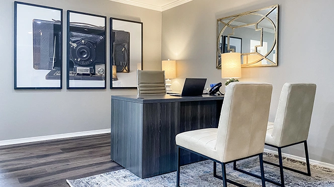 Office with grey wood l-shaped desk, two white guest chairs, artwork of old style camera