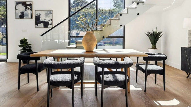 Modern dining room with large rectangular wooden table, six black boucle chairs and large open windows