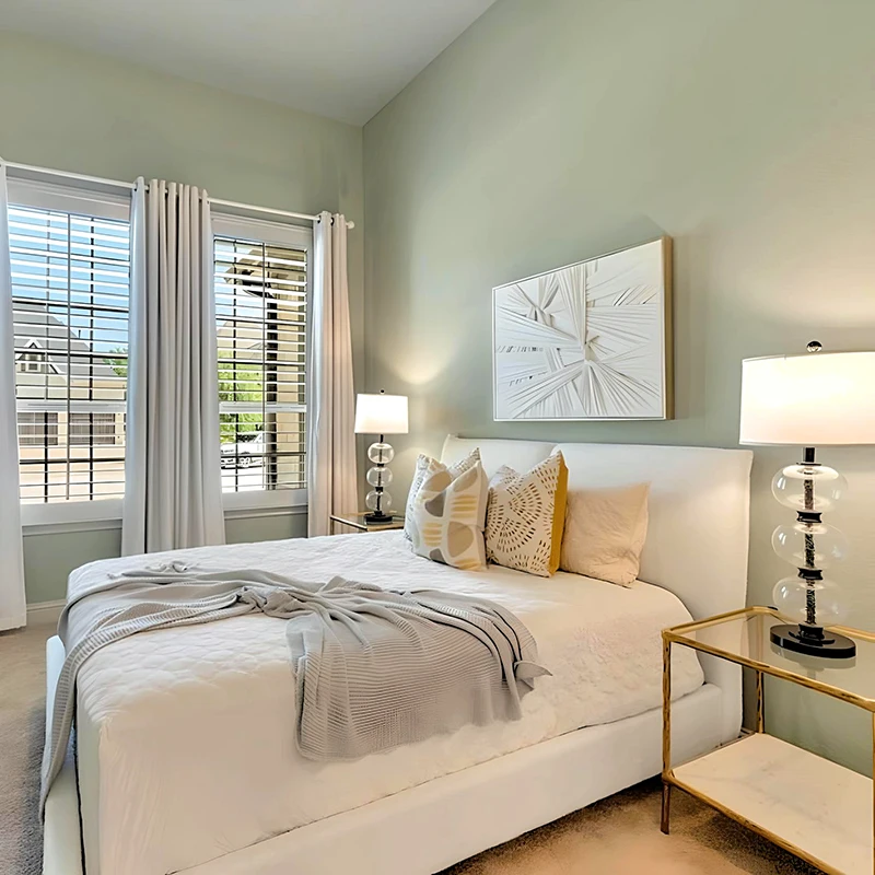 Bedroom with light green walls, white upholstered bed, white bedding, white abstract art, and glass lamps