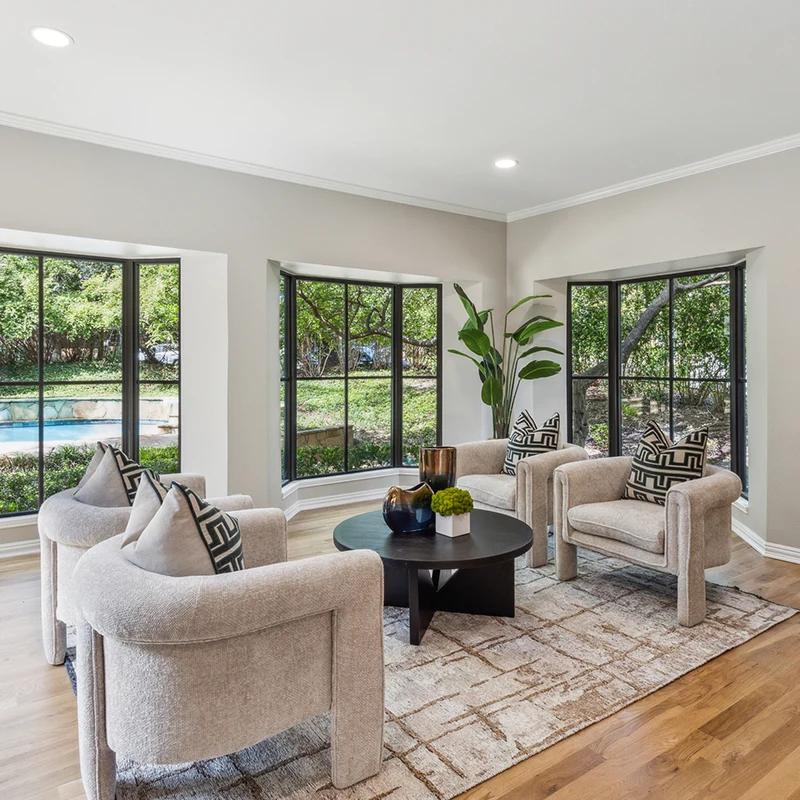Seating area with four modern light grey velvet chairs, small black round coffee table, black and white pillows