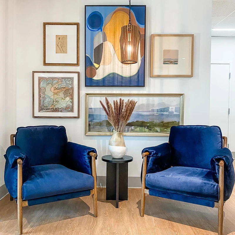 Seating area with two blue velvet chairs, small black table and five pieces of artwork creating a gallery wall