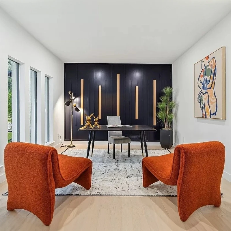 Home office with black accent wall, black desk, and two orange boucle sleek chairs