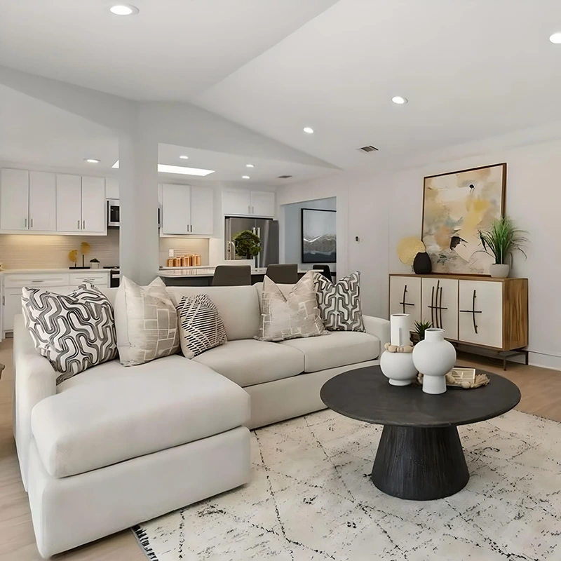 Living room with white l-shaped sofa, grey and black pillows, small round black coffee table and white accents