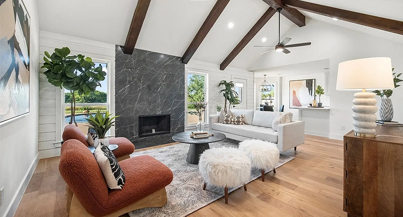 Living room with large grey marble fireplace, white modern sofa, two rust colored boucle chairs and two white fluffy ottomans