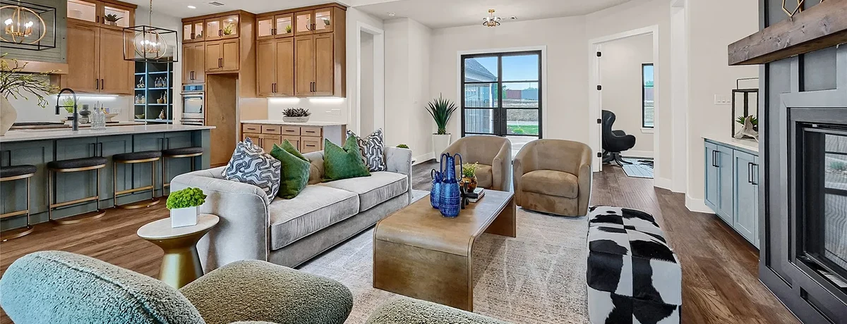 Living room with tan sofa and green pillows, two cozy green accent chairs and cowhide ottomans