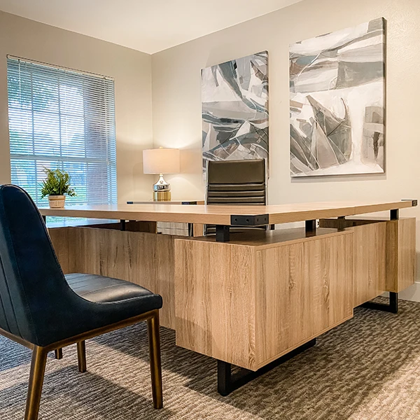 Office with light-colored wood l-shaped desk and abstract artwork