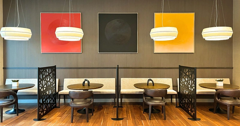 Reception seating area with white benches, leather low back chairs, round low hanging accent lighting and three red, black and yellow paintings