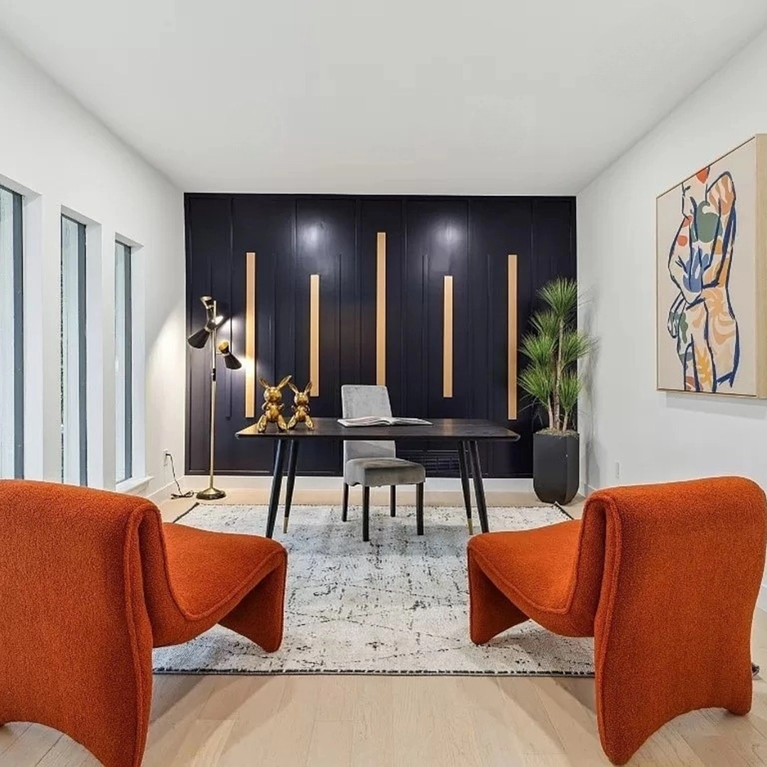 Modern home office with black accent wall, black desk, two velvet orange lounge chairs and colorful artwork