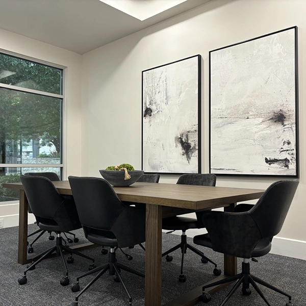 Conference room with large wooden table, six black chairs and abstract artwork