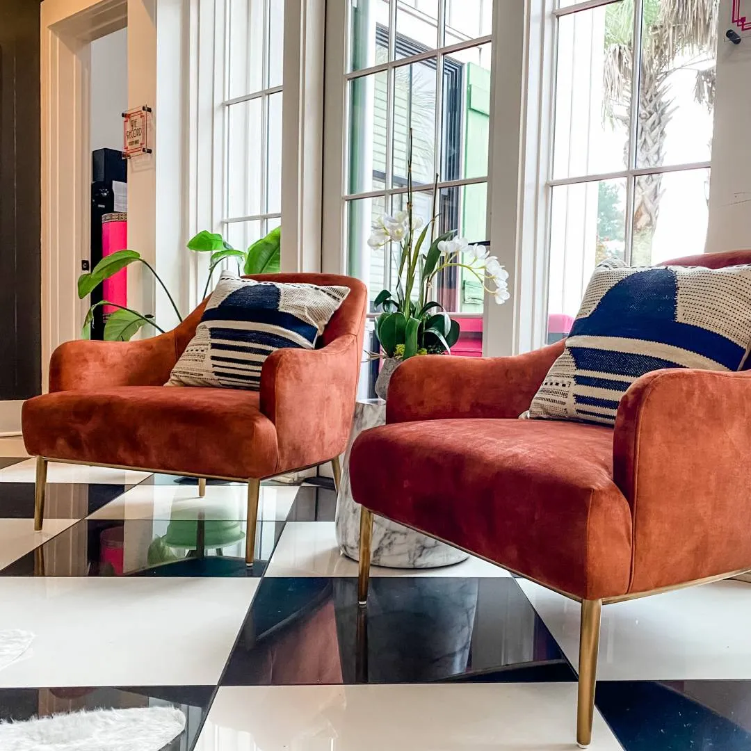Two orange velvet chairs with cream and blue pillows and a small accent table