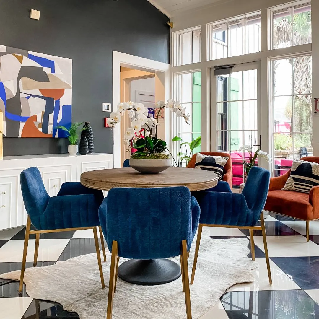 Round wooden dining table, four blue velvet chairs wtih gold accents and blue, white and orange abstract artwork