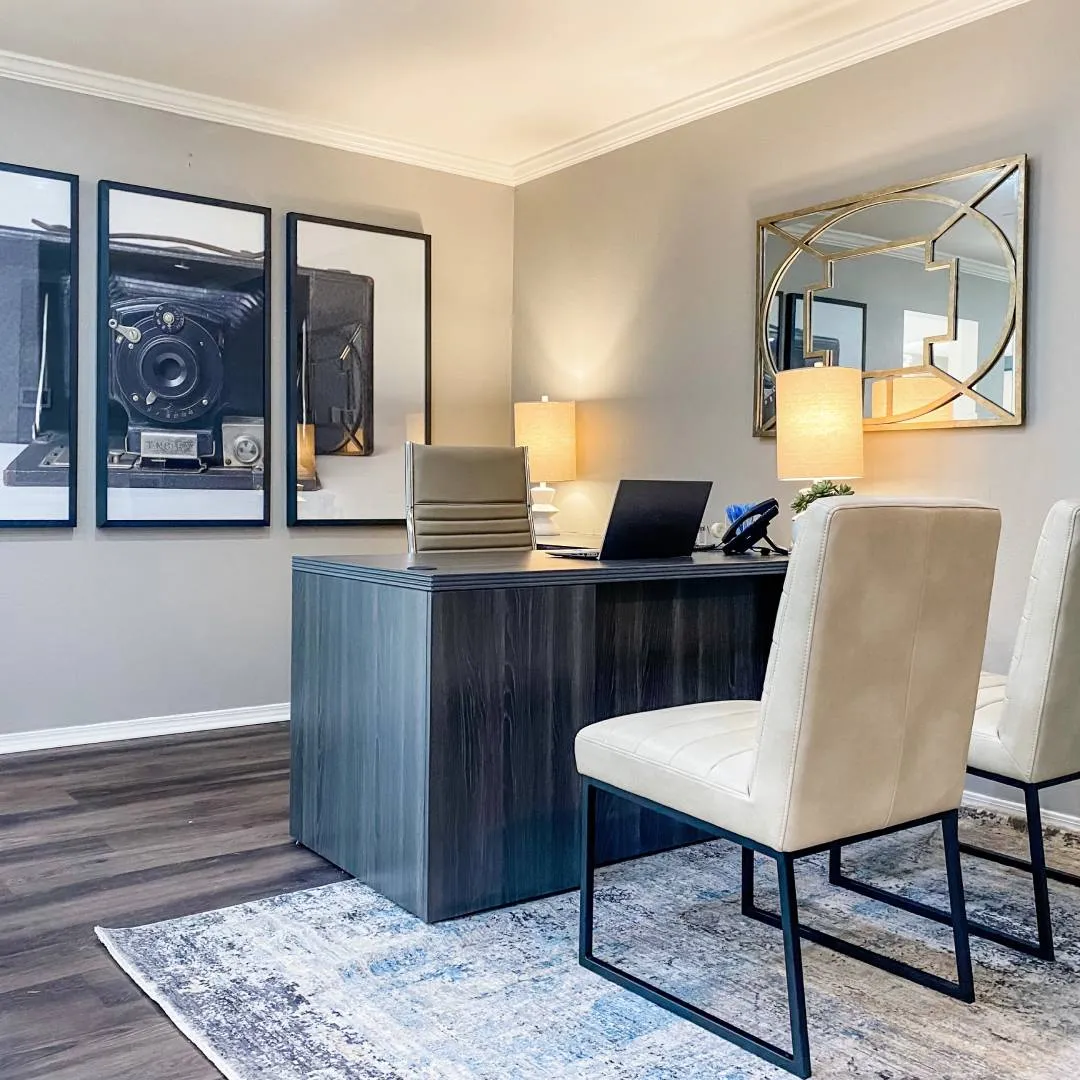 Leasing office with dark wood colored l-shaped desk, two cream colored leather chairs and photo of an old style camera behind desk