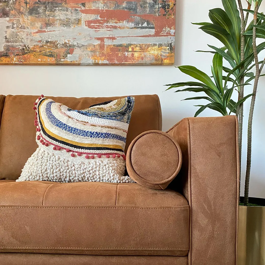 Close up of a canyon colored sofa with textured pillow and rustic colored artwork above the sofa
