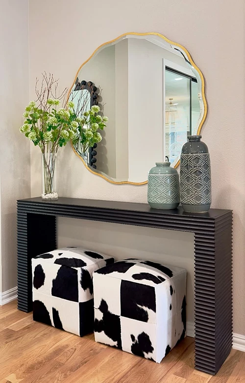 Black concole table with gold circle mirror and two cowhide ottomans