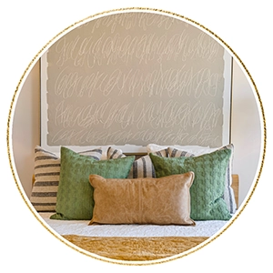 Close up of bed with green, gold and white linens and pillows, large artwork with cursive circles