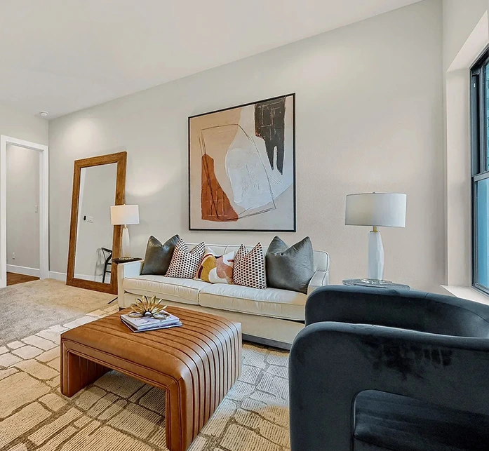 Staged seating area with sofa, lots of pillows, leather ottoman and large abstract artwork
